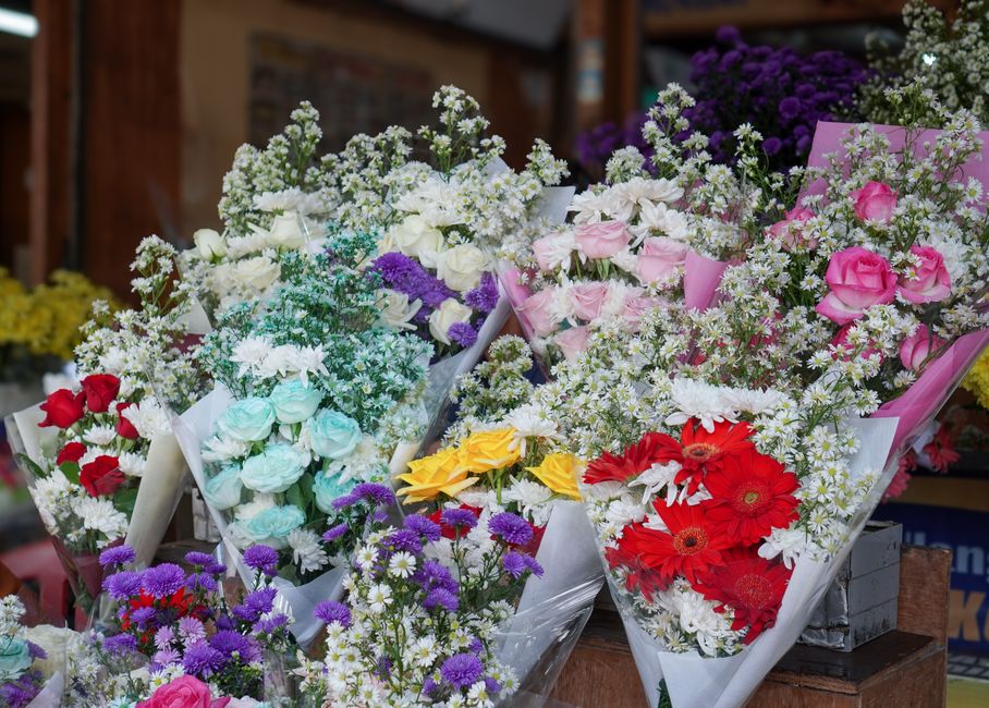 A vibrant display of floral bouquets arranged in white paper wrapping at Thornton Heath High Street florists, featuring a variety of fresh flowers including pink and white roses, red gerbera daisies, 